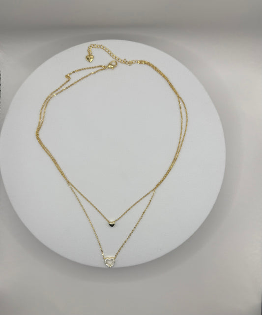Two gold necklaces on a white circular stand with a gray background